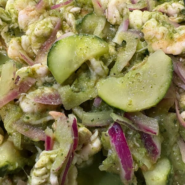 Close-up of Honduran ceviche with shrimp, red onions, and cucumbers in a green sauce.