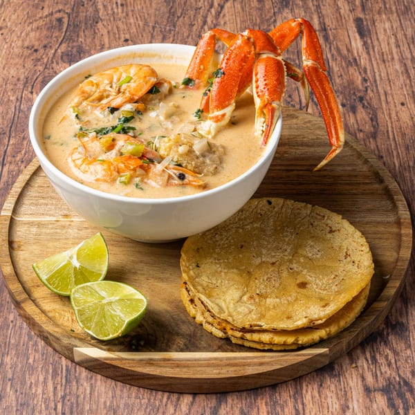 Honduran seafood soup with crab legs, shrimp, and vegetables, served with lime wedges and tortillas.