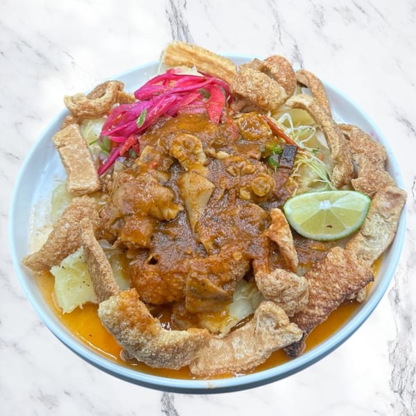Honduran dish with meat in sauce, pickled red onions, crispy pork rinds, and a lime wedge.