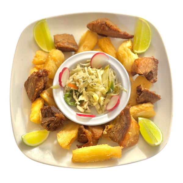 Honduran dish with fried pork, yuca, lime wedges, and a side of pickled cabbage salad.