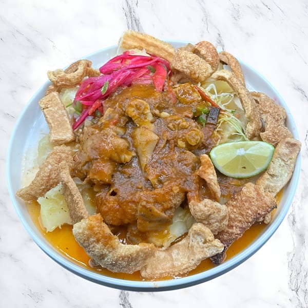Honduran dish with meat in sauce, pickled red onions, chicharrones, and a lime wedge.