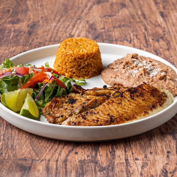 Grilled fish fillet with rice, refried beans, and a fresh salad with lime wedges.