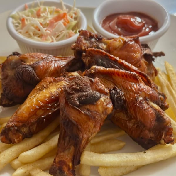 Crispy Honduran chicken wings and french fries with coleslaw and ketchup on a white plate.