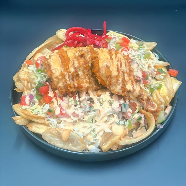 Honduran fried chicken with plantain chips, cabbage, tomato, and a creamy sauce on a dark plate.