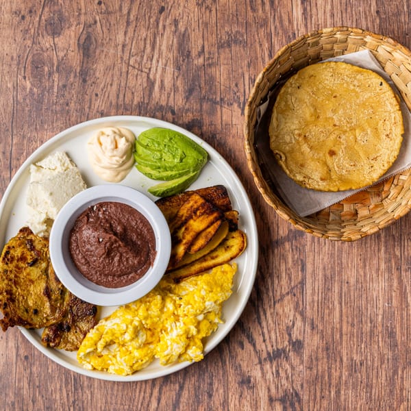 Honduran breakfast with scrambled eggs, steak, plantains, avocado, cheese, refried beans, and tortillas.