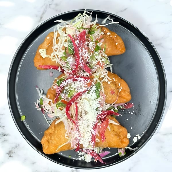 Three golden-fried Honduran empanadas topped with shredded cabbage, red onions, and crumbled white cheese.