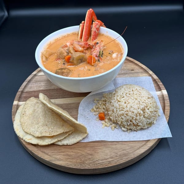 Honduran seafood soup with crab legs, shrimp, vegetables, rice, and tortillas on a wooden board.