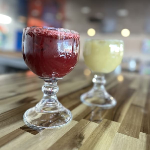 Two goblet glasses, one with red drink and the other with yellow, on a wooden table.