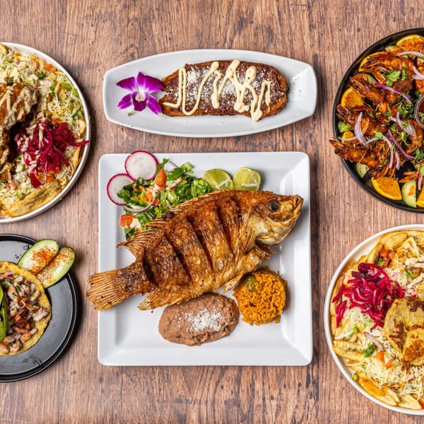 A Honduran feast with fried fish, plantains, shrimp, tacos, and various sides on a wooden table.