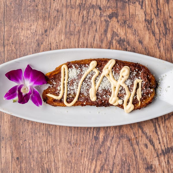 Honduran baleada with refried beans, cheese, and cream, garnished with a purple orchid on a white plate.