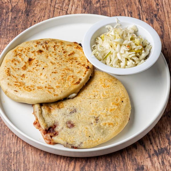 Two golden-brown Honduran pupusas with a side of curtido on a white plate.