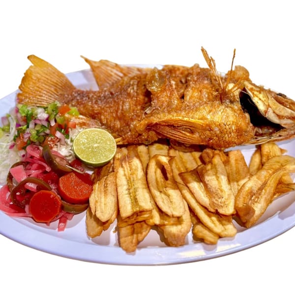 Whole fried fish with plantain chips, pico de gallo, pickled onions, and lime on a white plate.