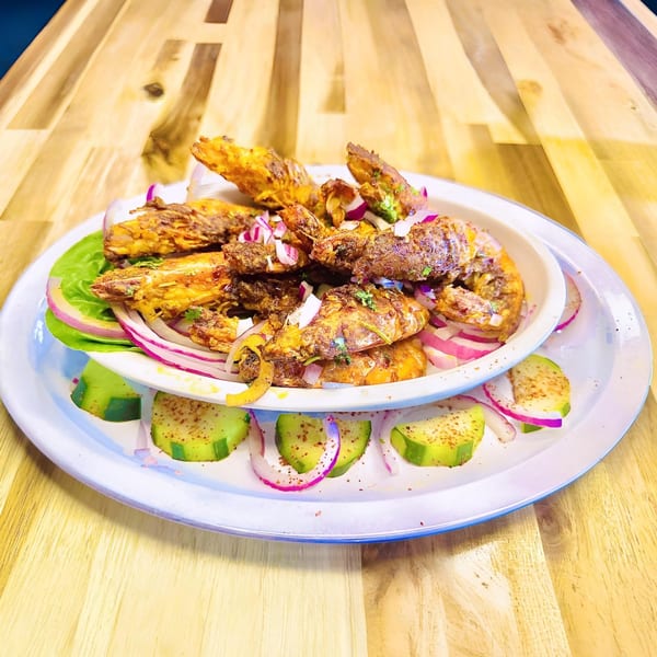 Honduran fried shrimp with red onions, lettuce, and cucumber slices on a white plate.