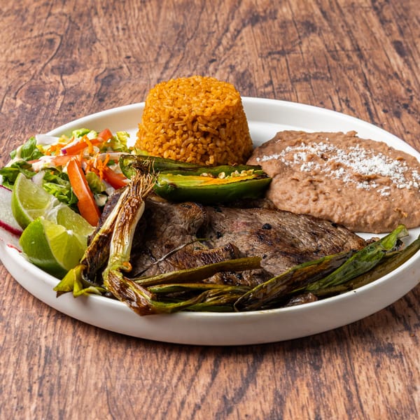 Honduran grilled steak with rice, refried beans, salad, grilled scallions, and jalapeño on a white plate.