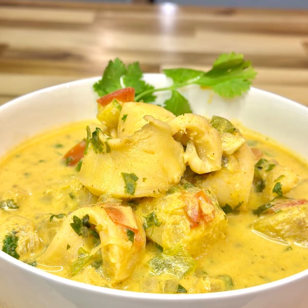 Honduran seafood soup with yellow broth, squid, red and green peppers, and cilantro in a white bowl.