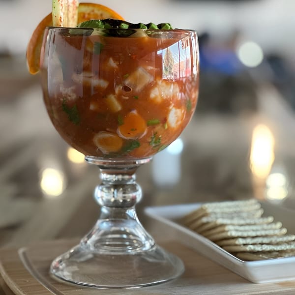 Honduran ceviche in a goblet, garnished with orange and avocado, served with crackers.