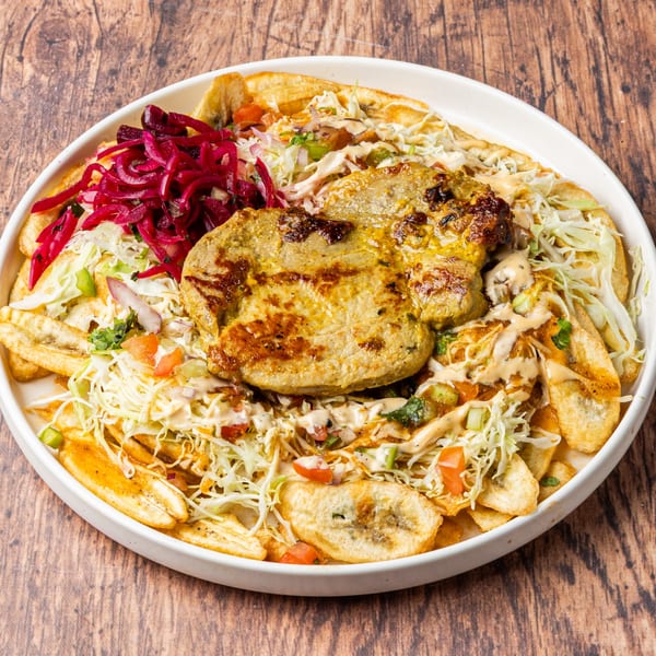 Honduran La Champa Latin Grill dish with grilled meat, plantain chips, cabbage, and pickled red onions.
