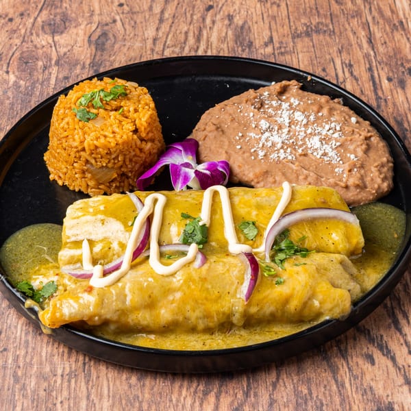 Honduran enchiladas with green sauce, red onions, rice, refried beans, and a purple orchid on a black plate.