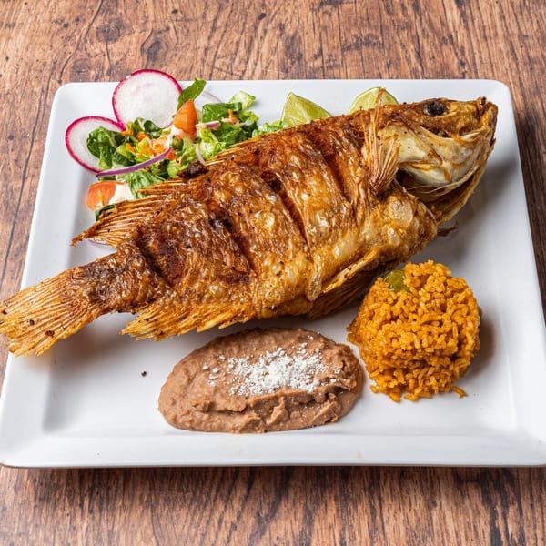 Whole fried fish with rice, refried beans, and a side salad with radishes and lime wedges.