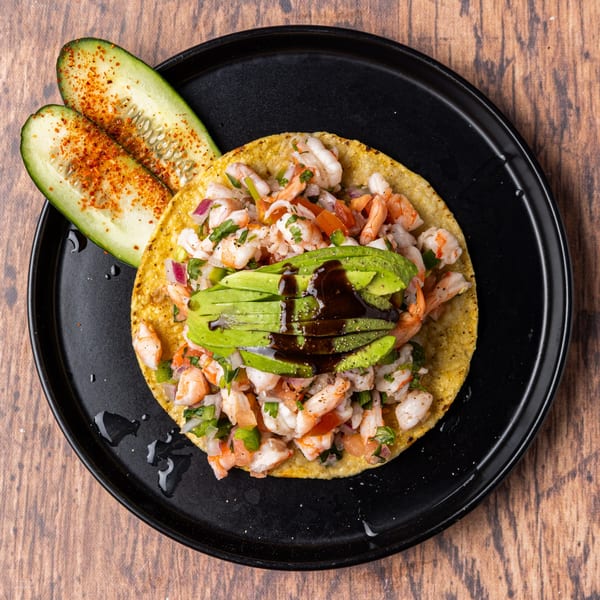 Honduran shrimp ceviche tostada with avocado and dark sauce, served with spiced cucumber slices.