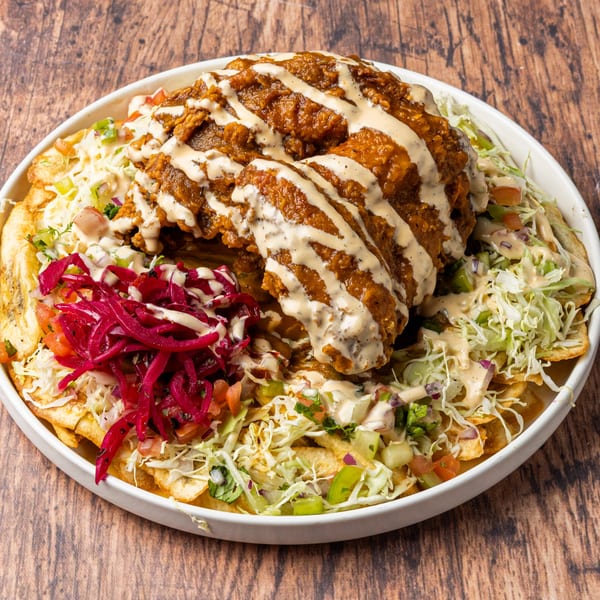 A Honduran dish with fried chicken, red cabbage, and white sauce on a bed of plantain chips.