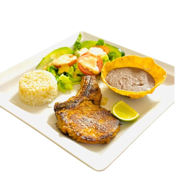 Honduran pork chop with rice, salad, refried beans in a tortilla bowl, and a lime wedge.